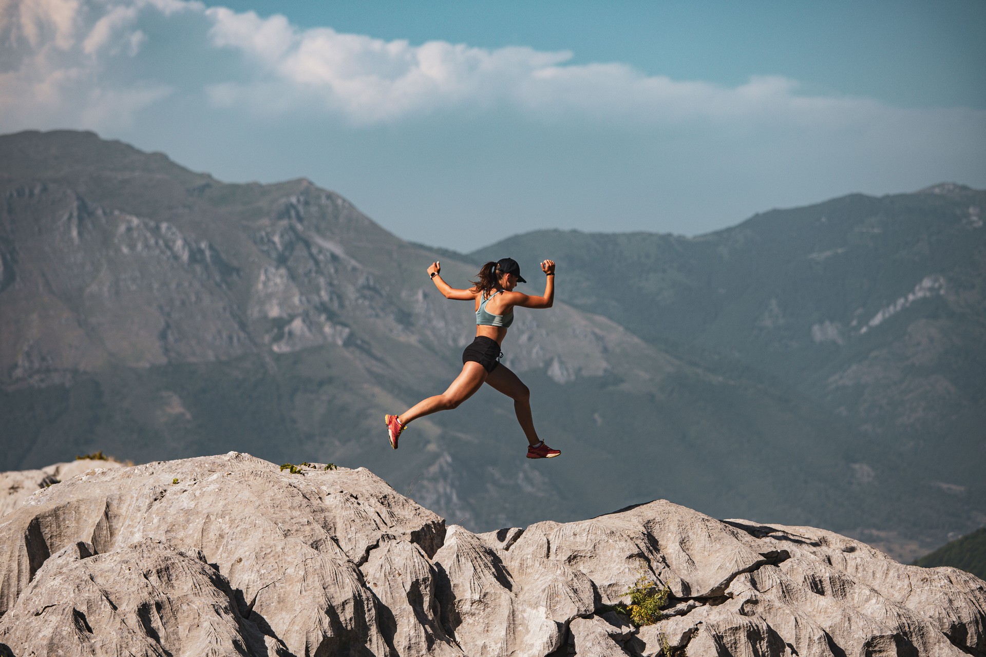 Woman leaping off cliffs wearing sports attire with distant mountains in the background