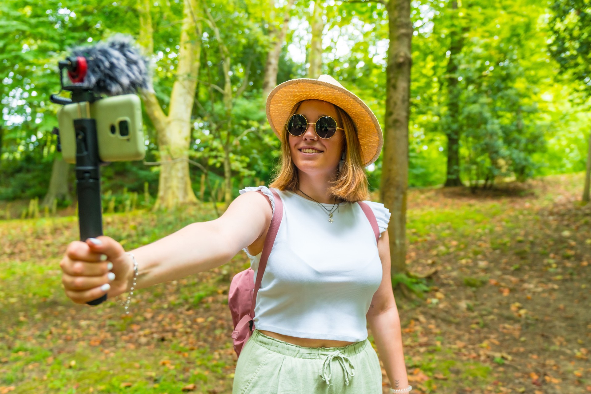 Cheerful young female vlogger recording vlog and going live during hiking adventure